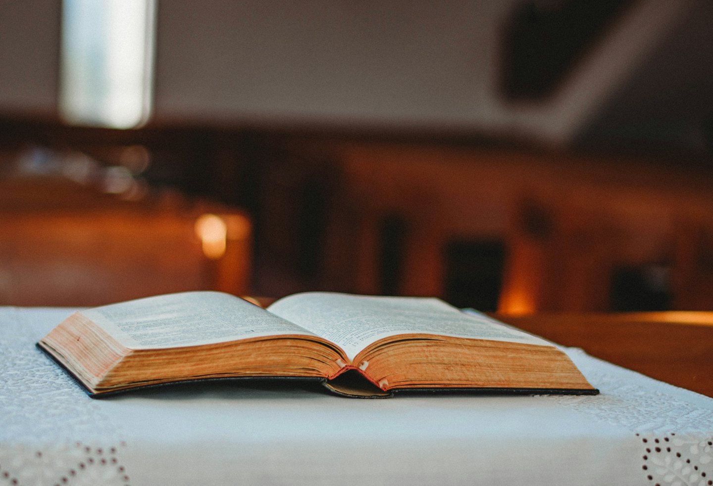 Un libro antico aperto con pagine dorate su una tovaglia di pizzo.